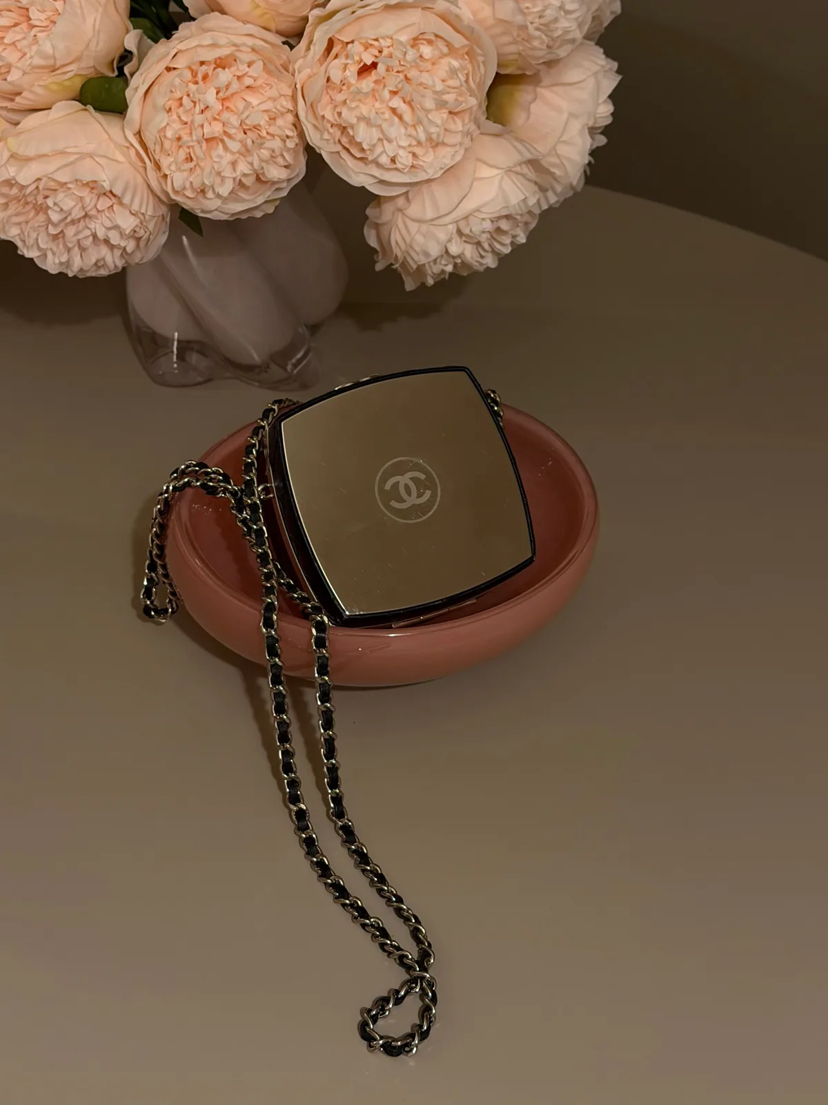 Chanel mirror pouch and chain beside pale peonies